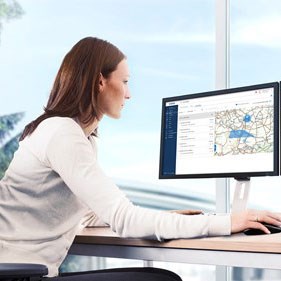 A fleet manager sits in her office and looks with interest at a screen on which VDO software is running. You can see a menu and a section of a map.