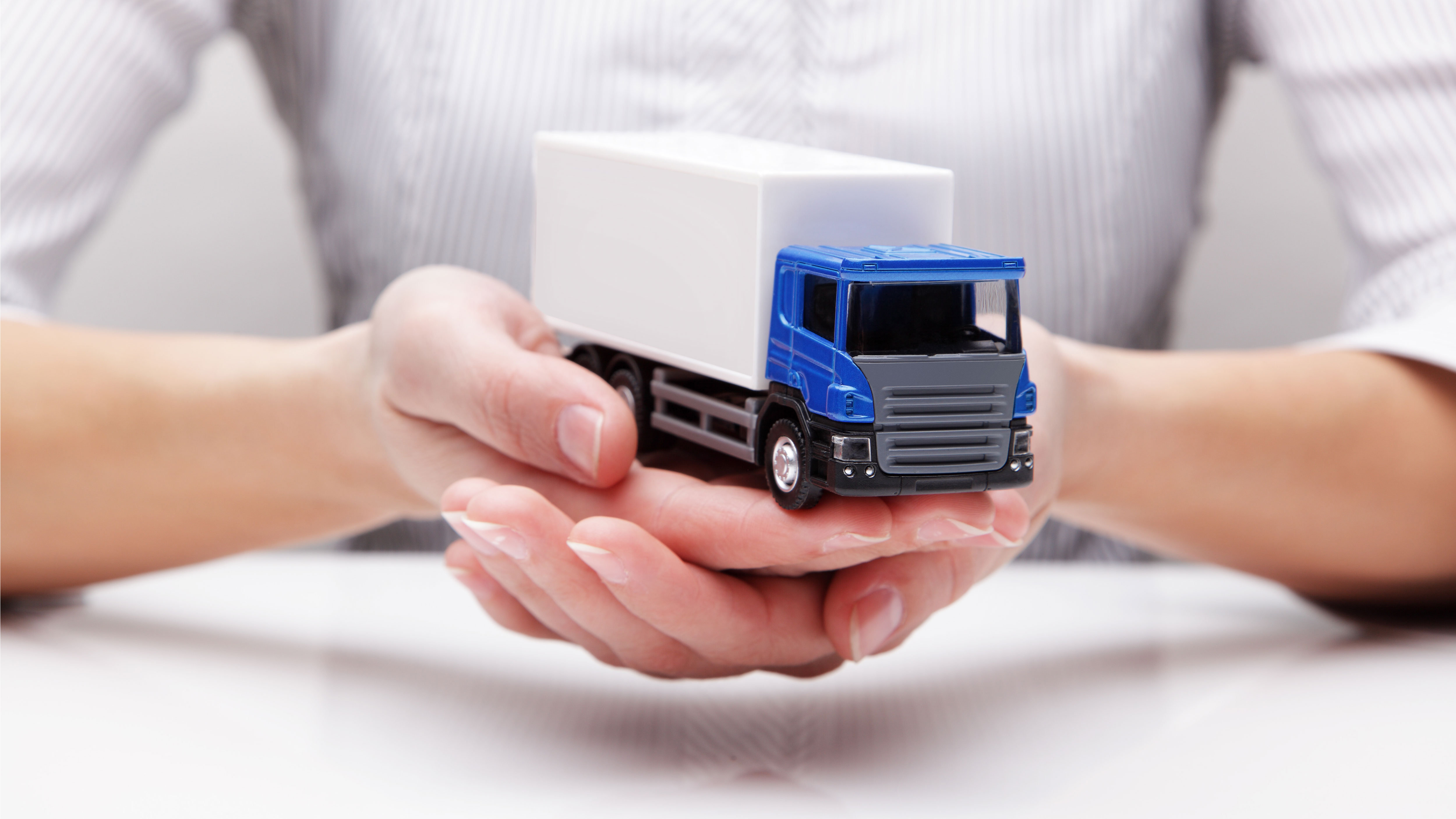A person in a white shirt carefully holds a toy truck in both hands. The cab of the truck is the typical blue color of VDO.